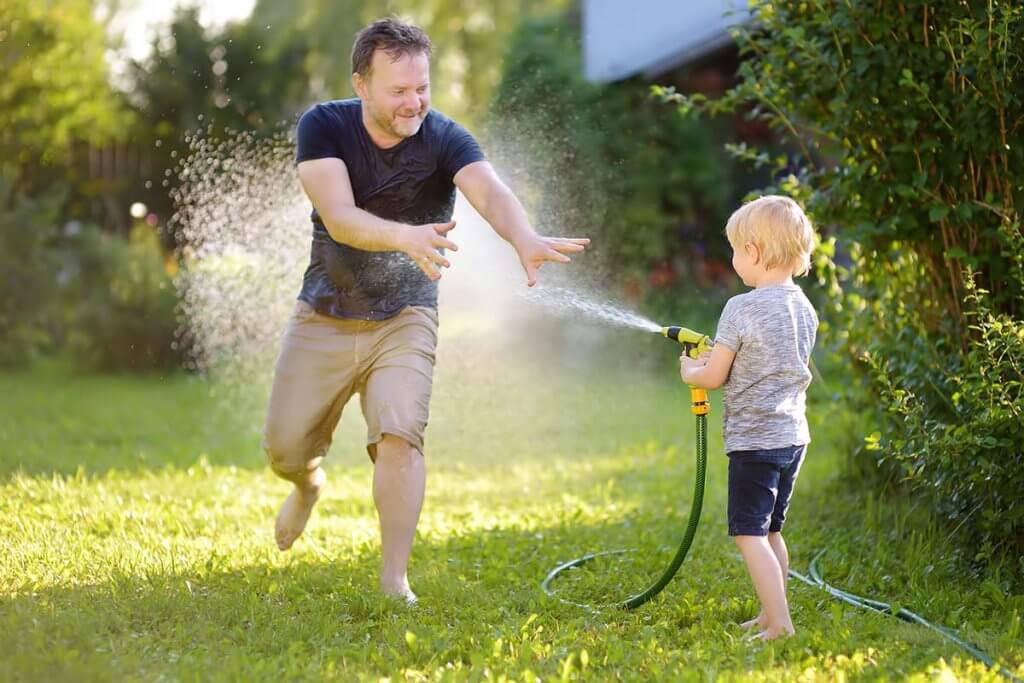 Kind spritzt Vater mit Gartenschlauch ab