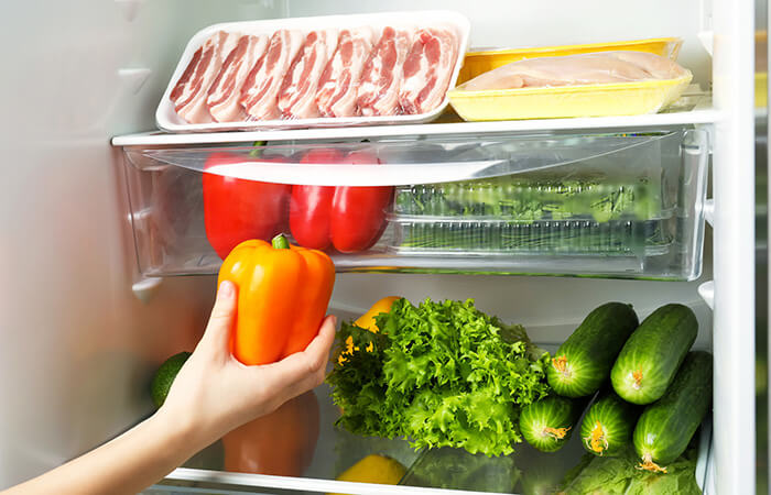 Hand greift im Kühlschrank nach Paprika