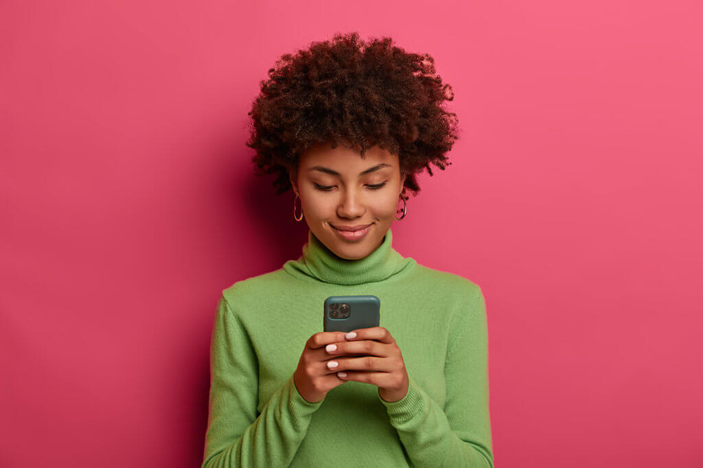 junge Person mit Smartphone in der Hand vor pinker Wand