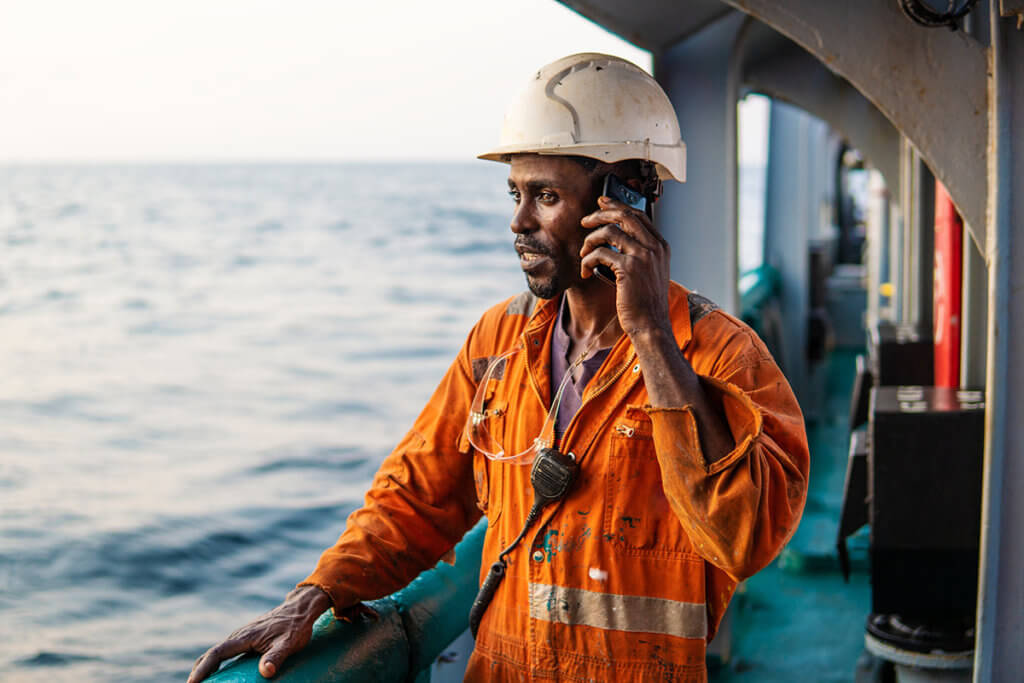 Person in Arbeitskluft auf Frachtschiff mit Smartphone in der Hand