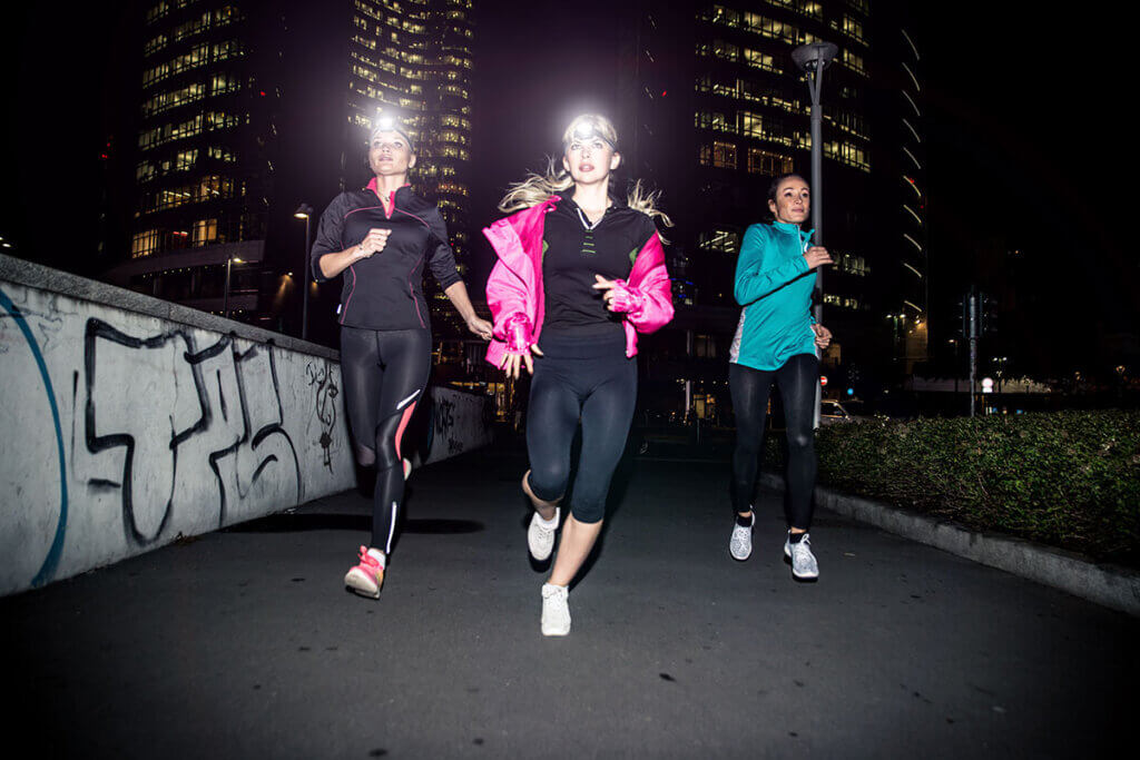 drei Frauen joggen in Dunkelheit mit Stirnlampen