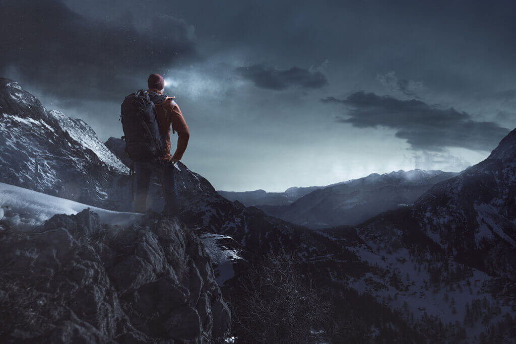 Mann wandert nachts mit Stirnlampe an Bergklippe