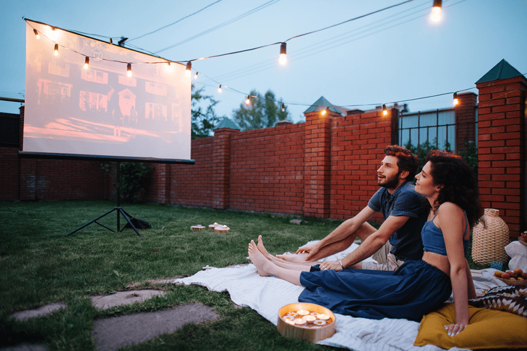 paar sitzt im garten und sieht film per tageslichtbeamer an leinwand