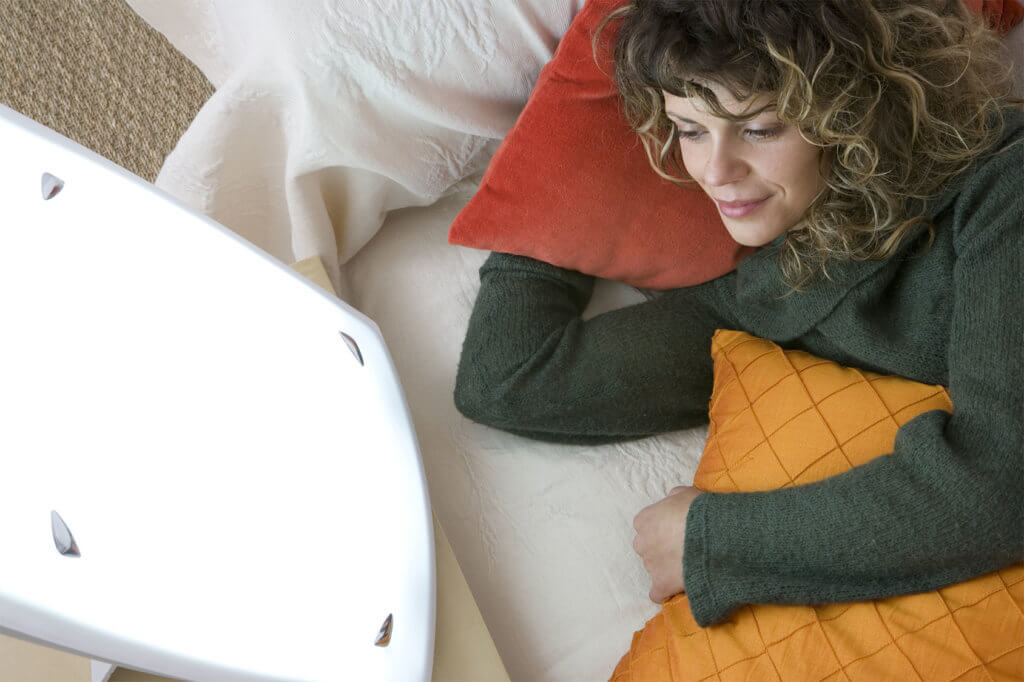 Frau liegt im Bett mit Tageslichtlampe