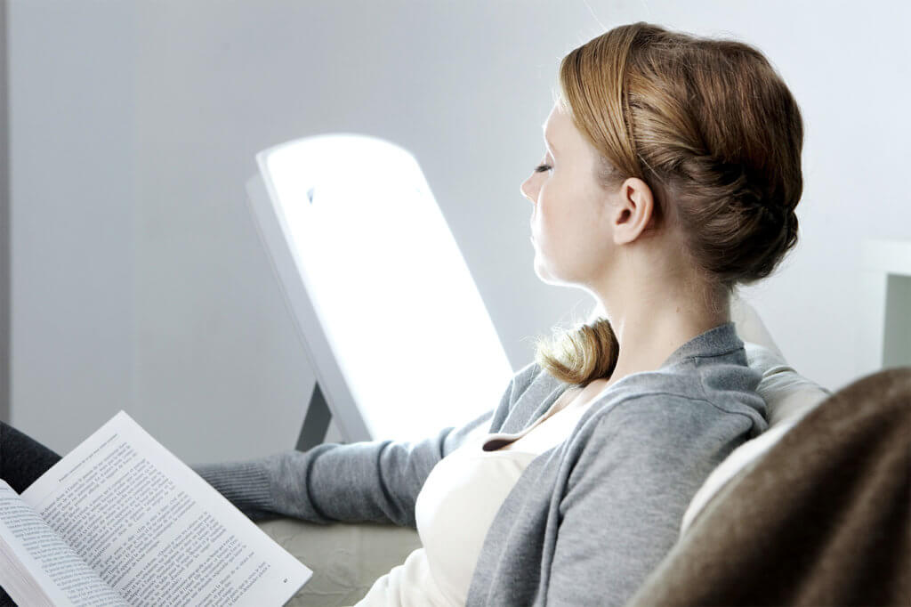 Frau liest ein Buch mit Tageslichtlampe