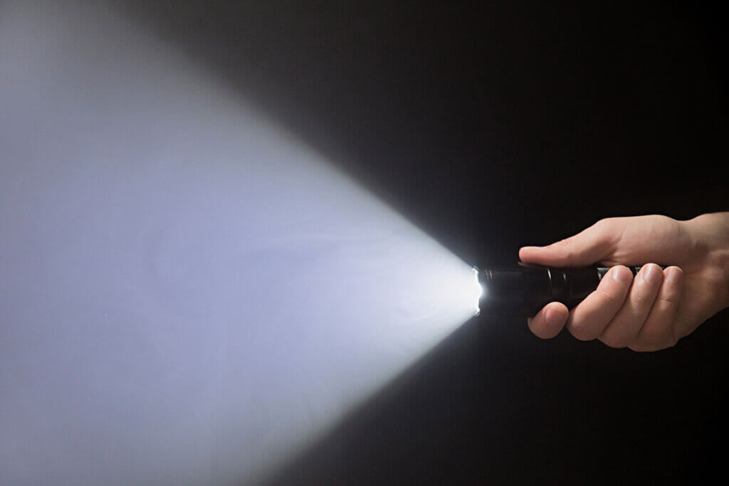 hand haelt angschaltete taschenlampe im dunkeln, lichtstrahl mit weitem abstrahlwinkel sichtbar