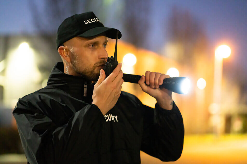 sicherheitsperson am abend mit taschenlampe spricht in walkie talkie
