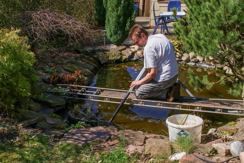 Mann reinigt Gartenteich mit Teichschlammsauger