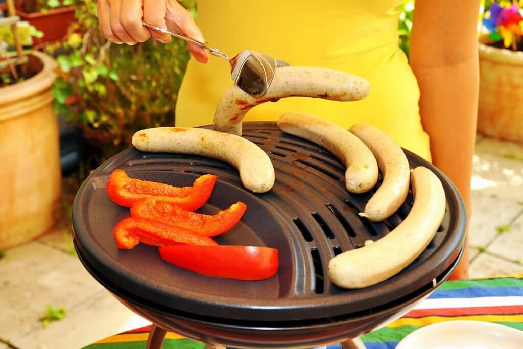 frau bereitet wurst und gemuese auf tischgasgrill zu