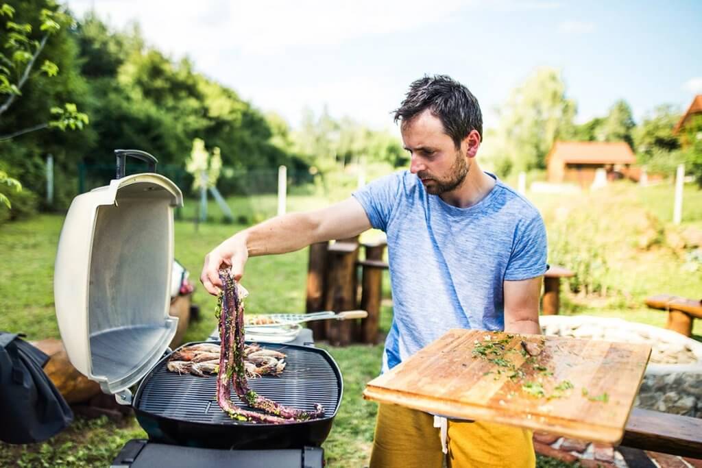 mann mittleren alters bereitet meeresfruechte auf tischgasgrill zu