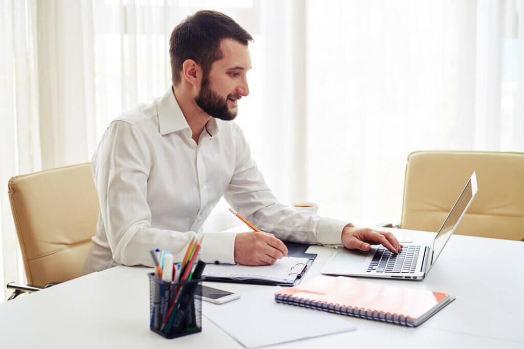 Mann arbeitet am Tisch mit Ultrabook und Notizen