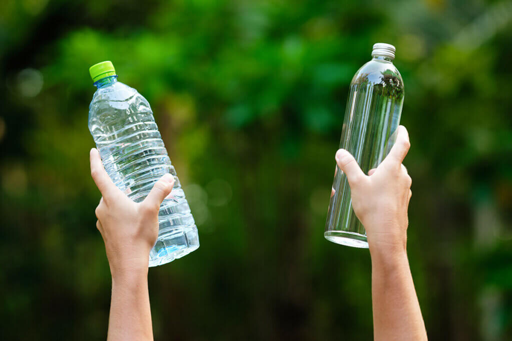 Hände halten Plastik- und Glasflasche hoch