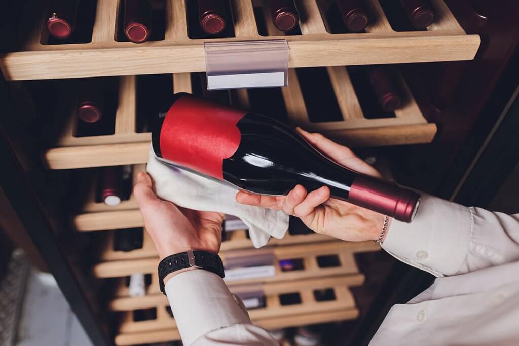 Person entnimmt Flasche Wein aus Weinkuehlschrank